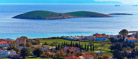A coastal town with buildings, green fields, and a view of the sea and distant mountains.