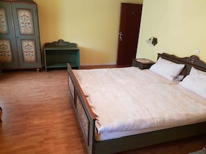 Un dormitorio con una cama de madera, una mesita de noche verde, un armario de madera y una puerta.