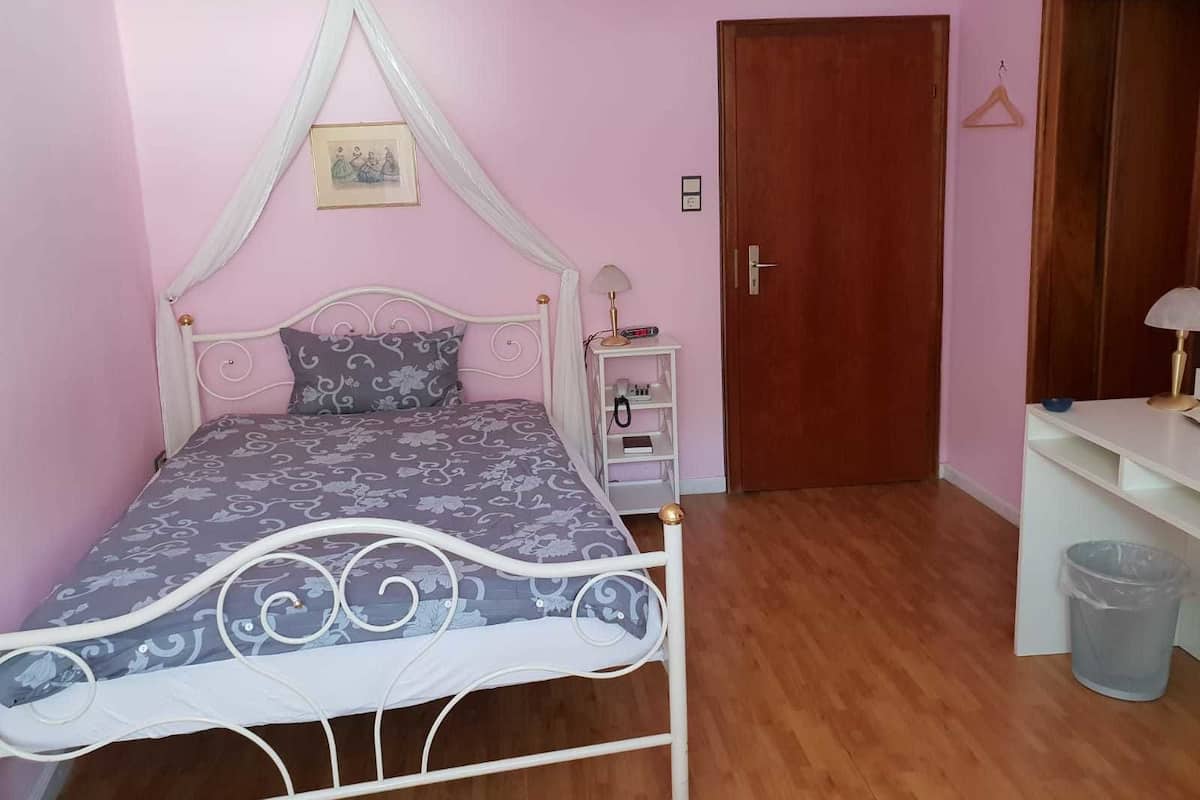 A bedroom with a canopy bed, a bedside table with a lamp, a wooden door, and a white wardrobe.