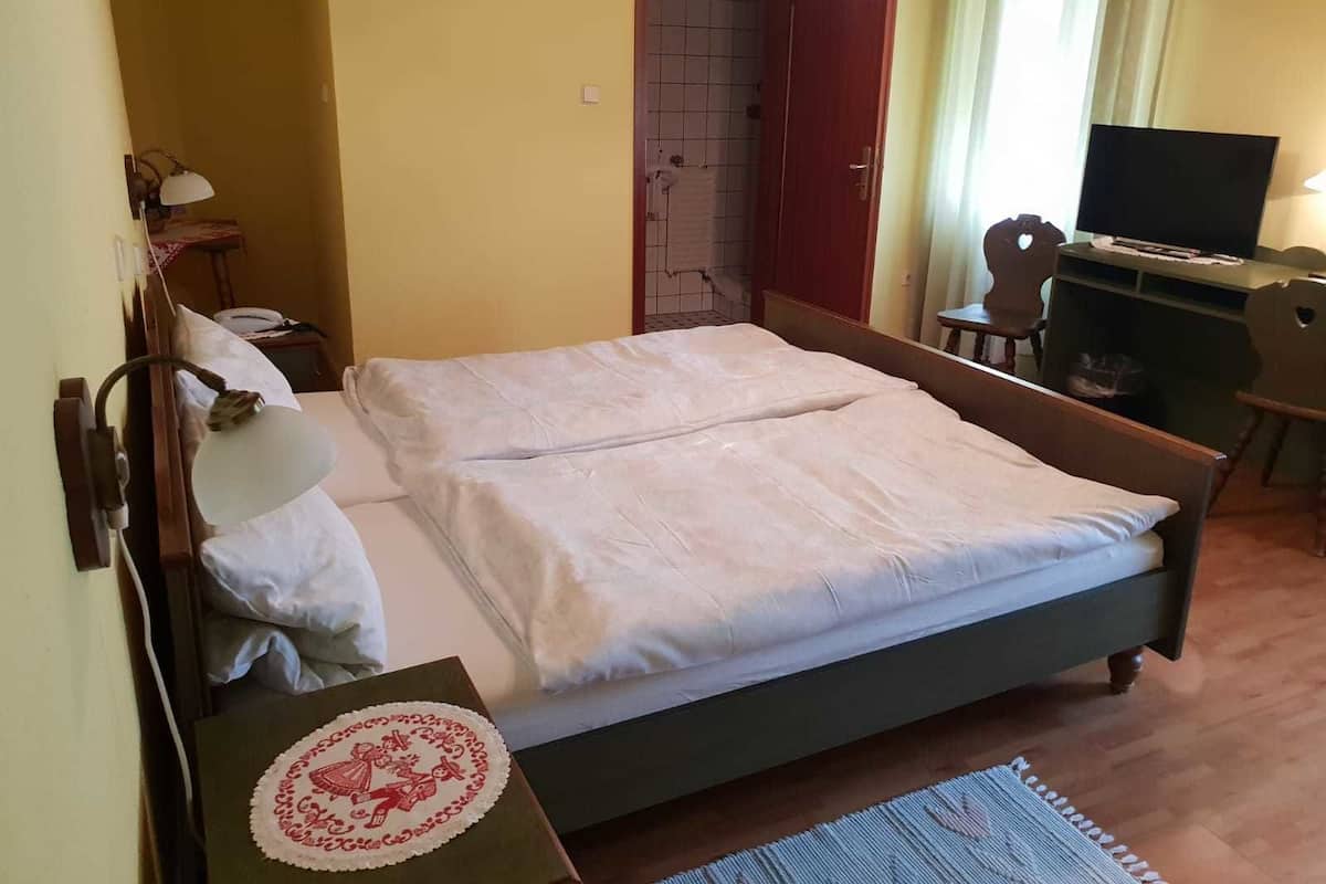 A neatly made bed with a white duvet, a bedside table with a lamp, a desk with a computer, and a chair.