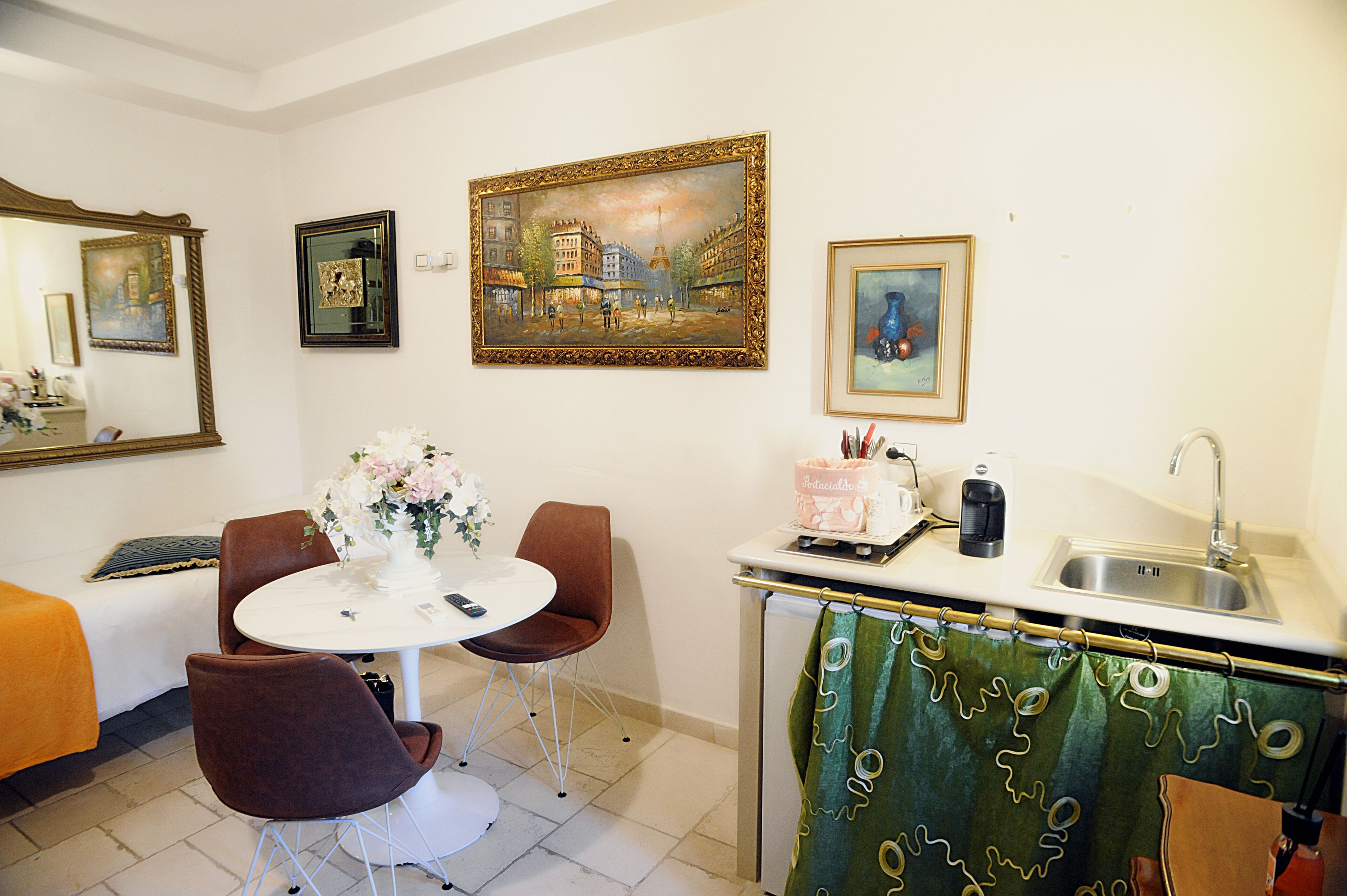 A room with a dining table, chairs, a small kitchen area with a sink, and a green curtain.