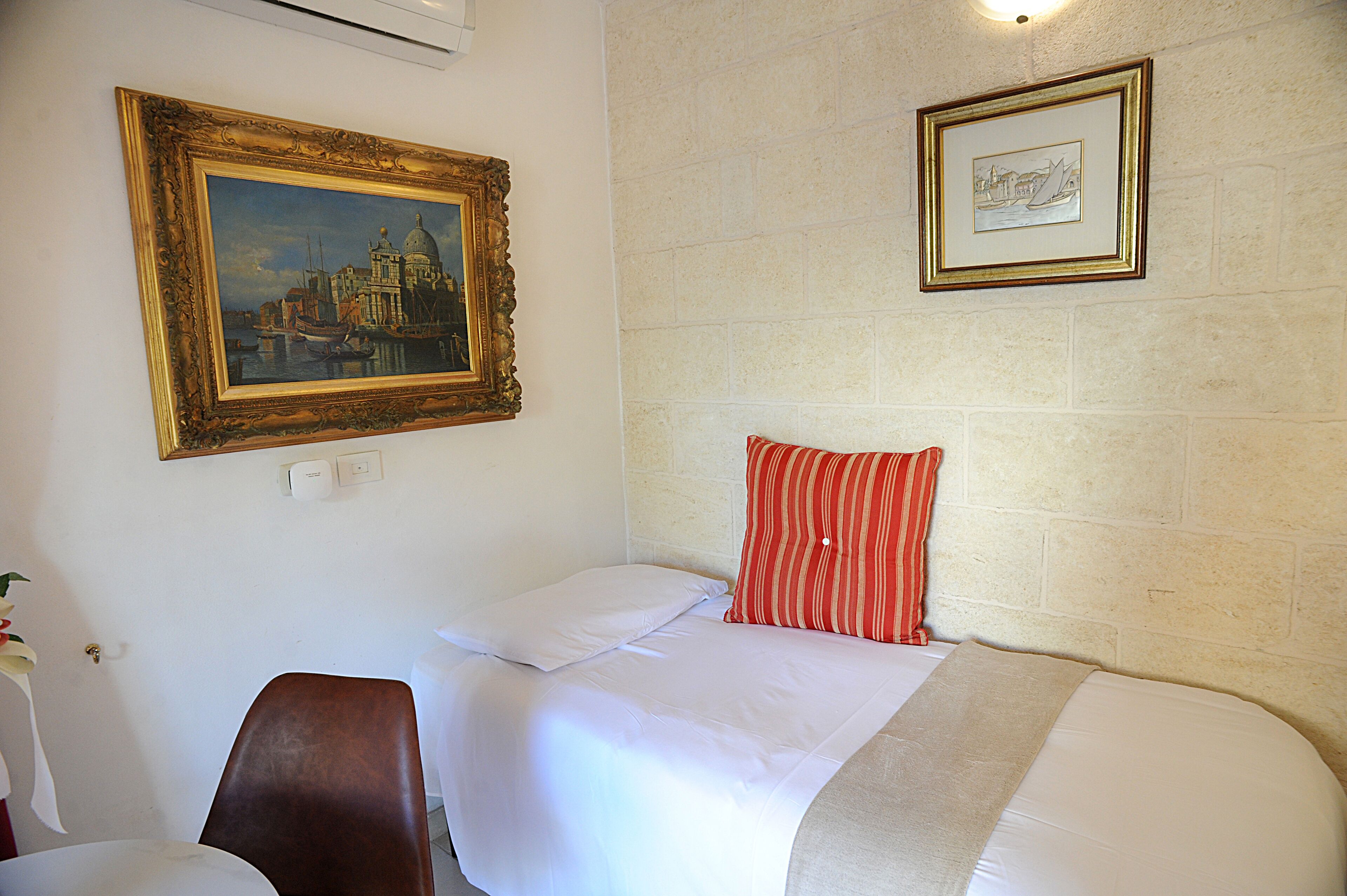 Habitación de hotel con una cama, una silla, un cuadro y una fotografía enmarcada en la pared.