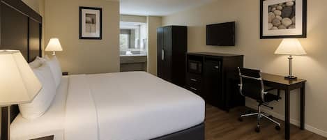 A hotel room with a large bed, a desk, a chair, a television, and a framed picture on the wall.