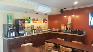 A café with a coffee machine, waffle maker, and a juice dispenser. There are tables and chairs for seating.