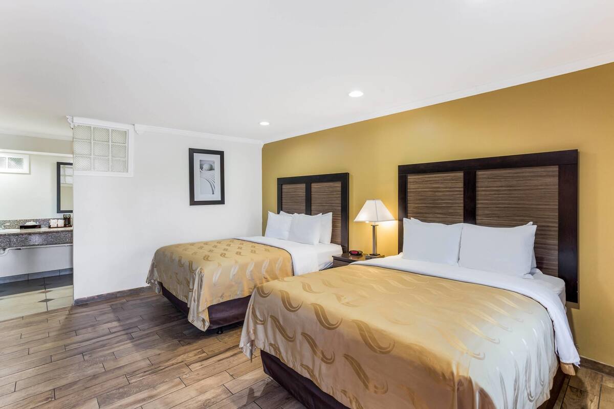 Habitación de hotel con dos camas, un baño con lavamanos y un espejo.