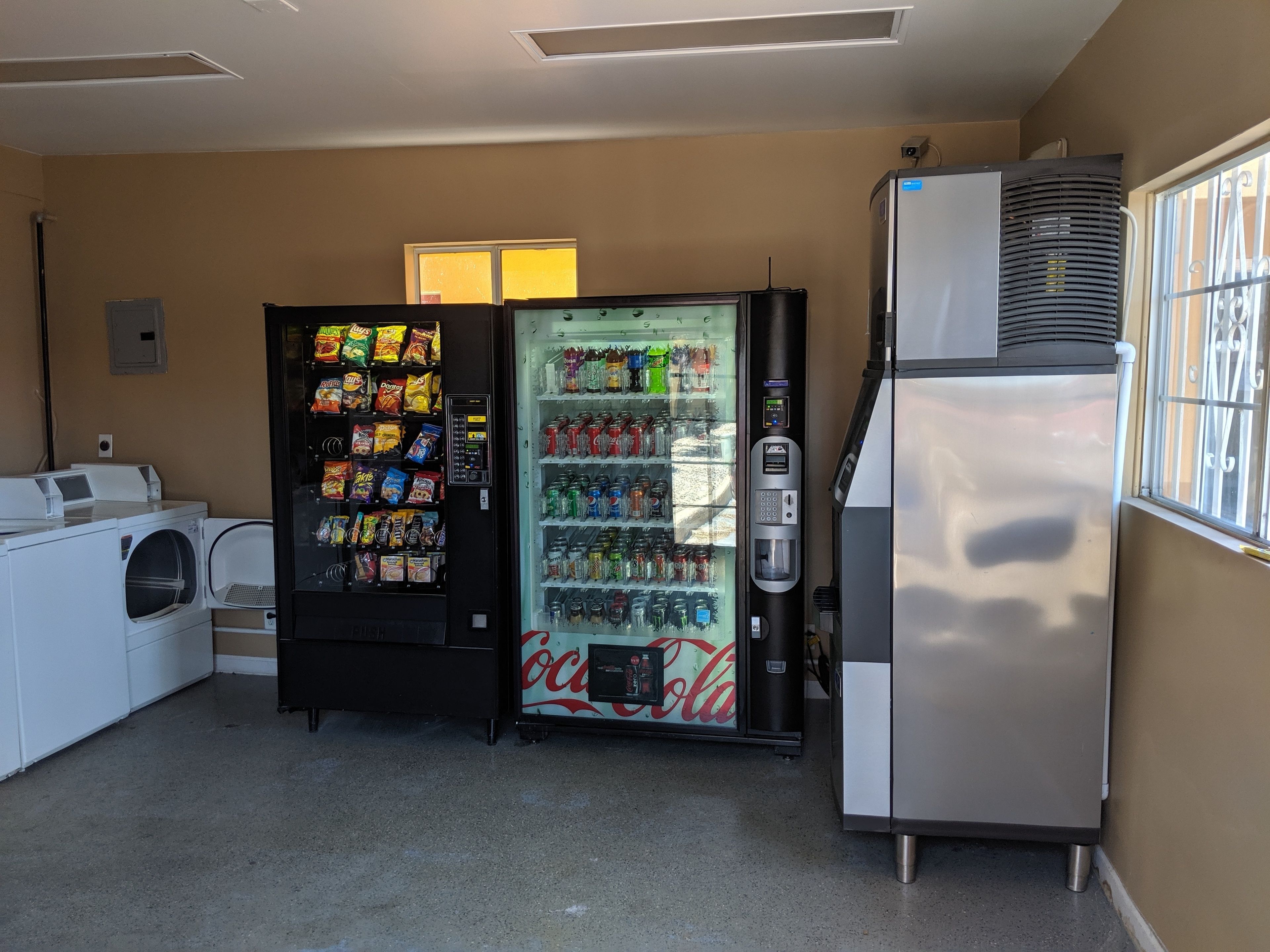 A laundry area with a vending machine and a refrigerator.
