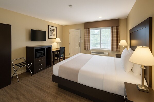 A hotel room with a large bed, a desk with a chair, a television, and a window with curtains.