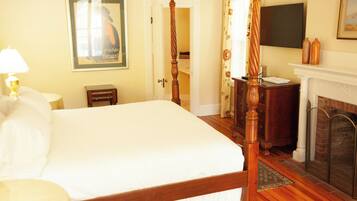A hotel room with a large bed, a wooden four-poster bed, a fireplace, a television mounted on the wall, and a framed picture on the wall.