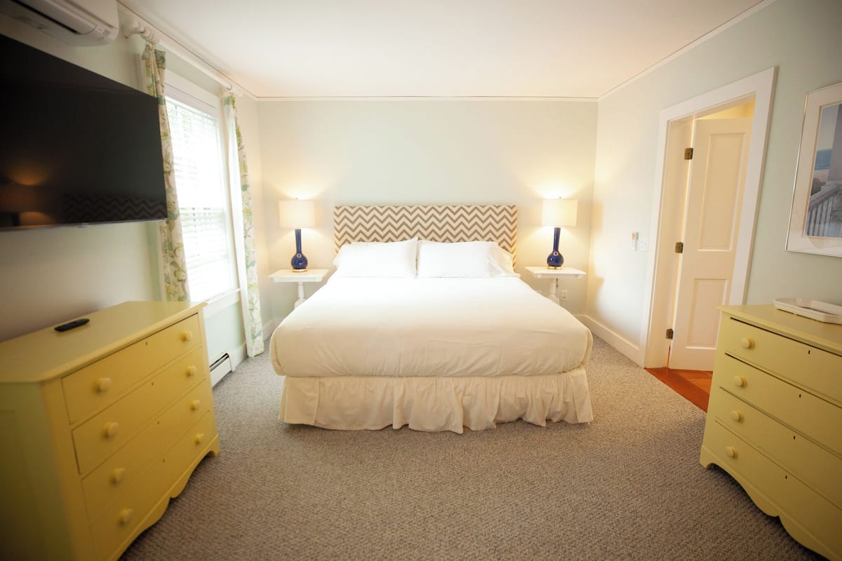 A bedroom with a bed, two bedside tables, a TV, and a door.