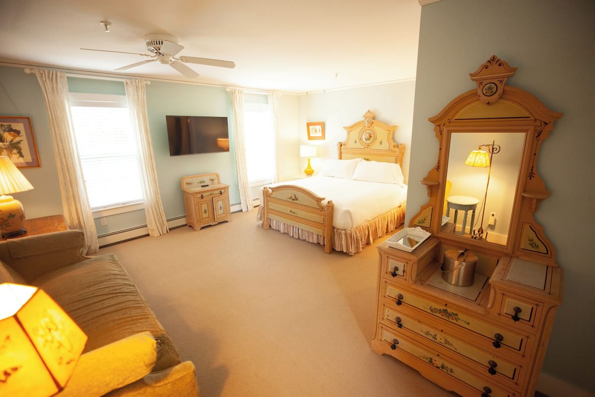 A bedroom with a bed, dresser, vanity, and a ceiling fan.