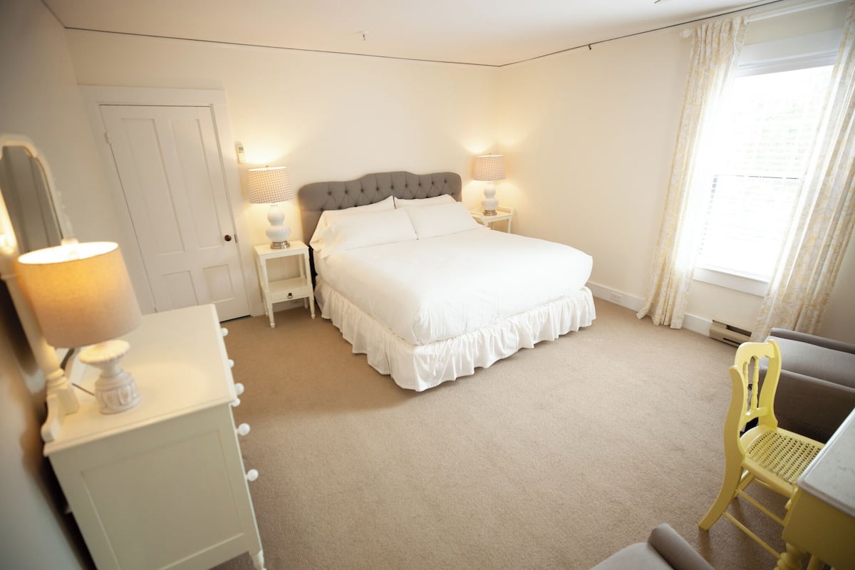 A neatly arranged bedroom with a large bed, bedside lamps, a chair, and a desk.
