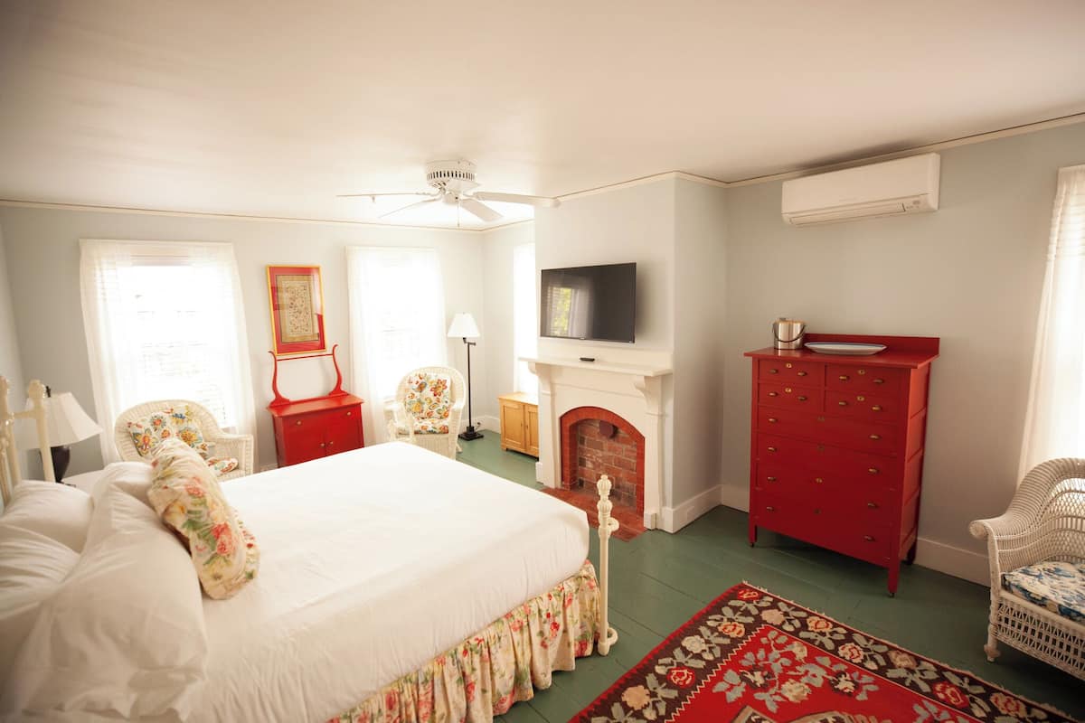 A bedroom with a bed, a red dresser, a television, a fireplace, and wicker chairs.