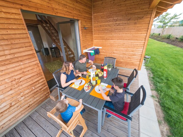 A wooden deck with a table set for a meal, surrounded by chairs.