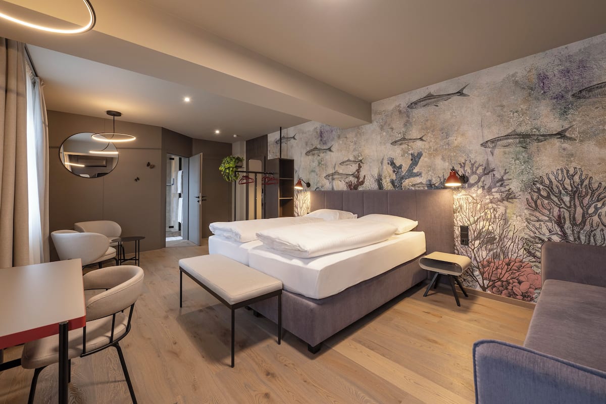 A modern hotel room with a bed, seating area, and a wall mural.
