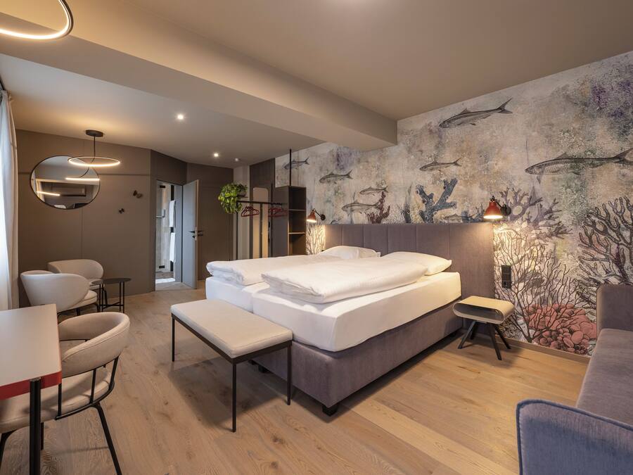 A modern hotel room with a bed, seating area, and a wall mural.