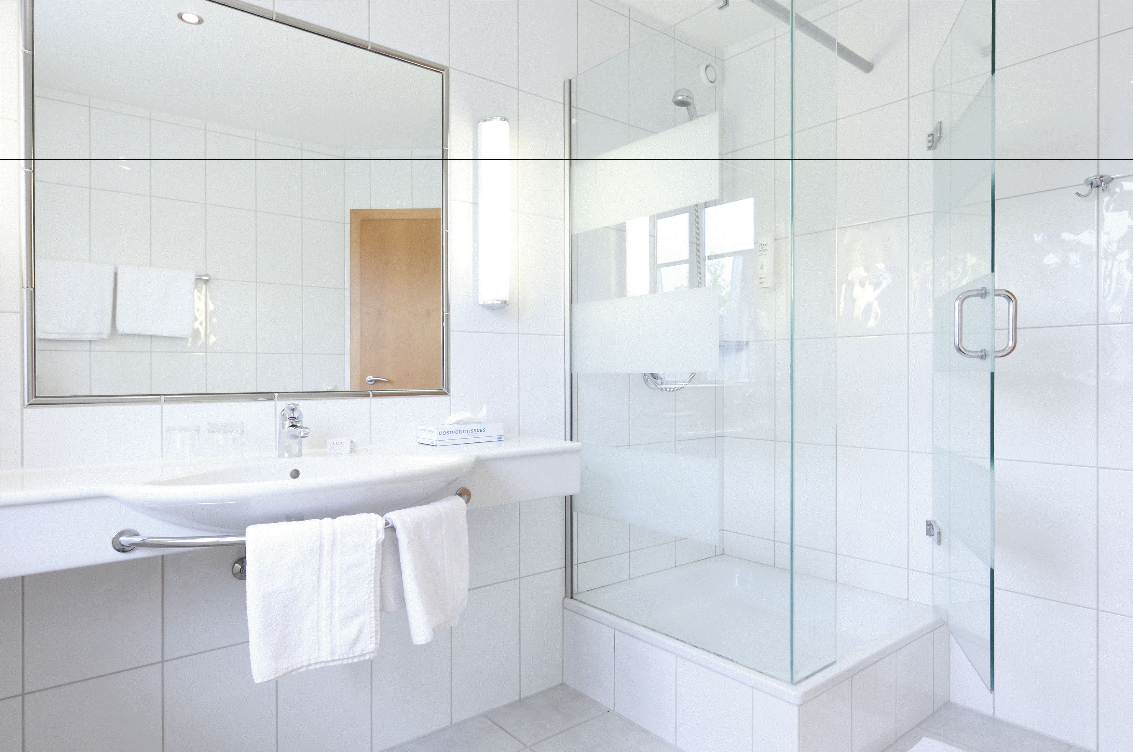 A modern bathroom with a glass-enclosed shower, a white sink, and a large mirror.