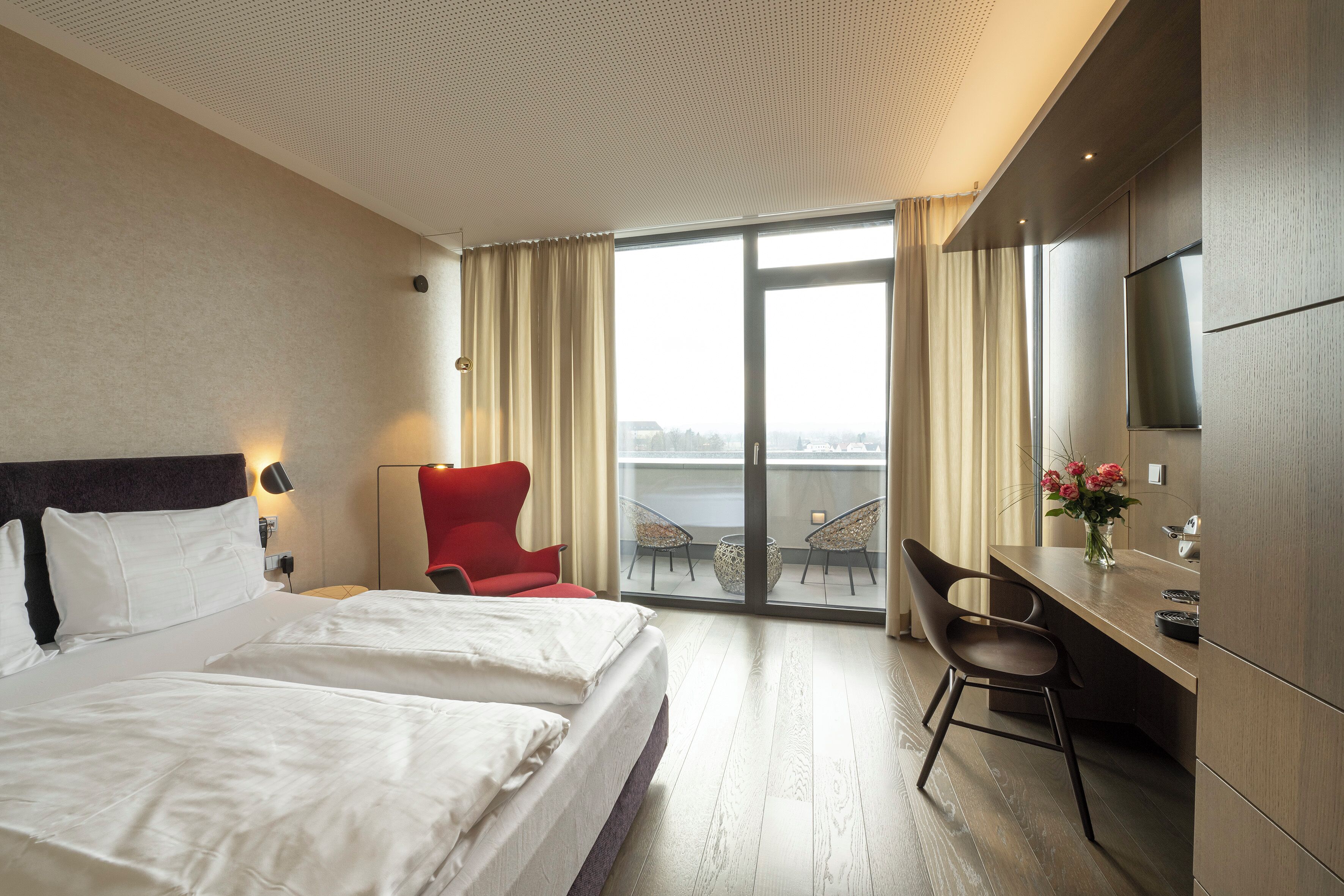 A hotel room with a bed, a desk, a chair, a TV, and a view of the city.