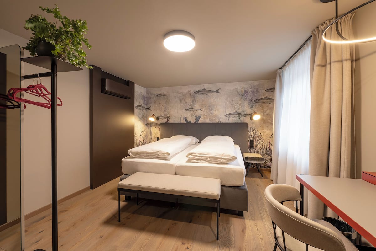 A hotel room with a bed, bedside table, bench, and a wall with fish mural.