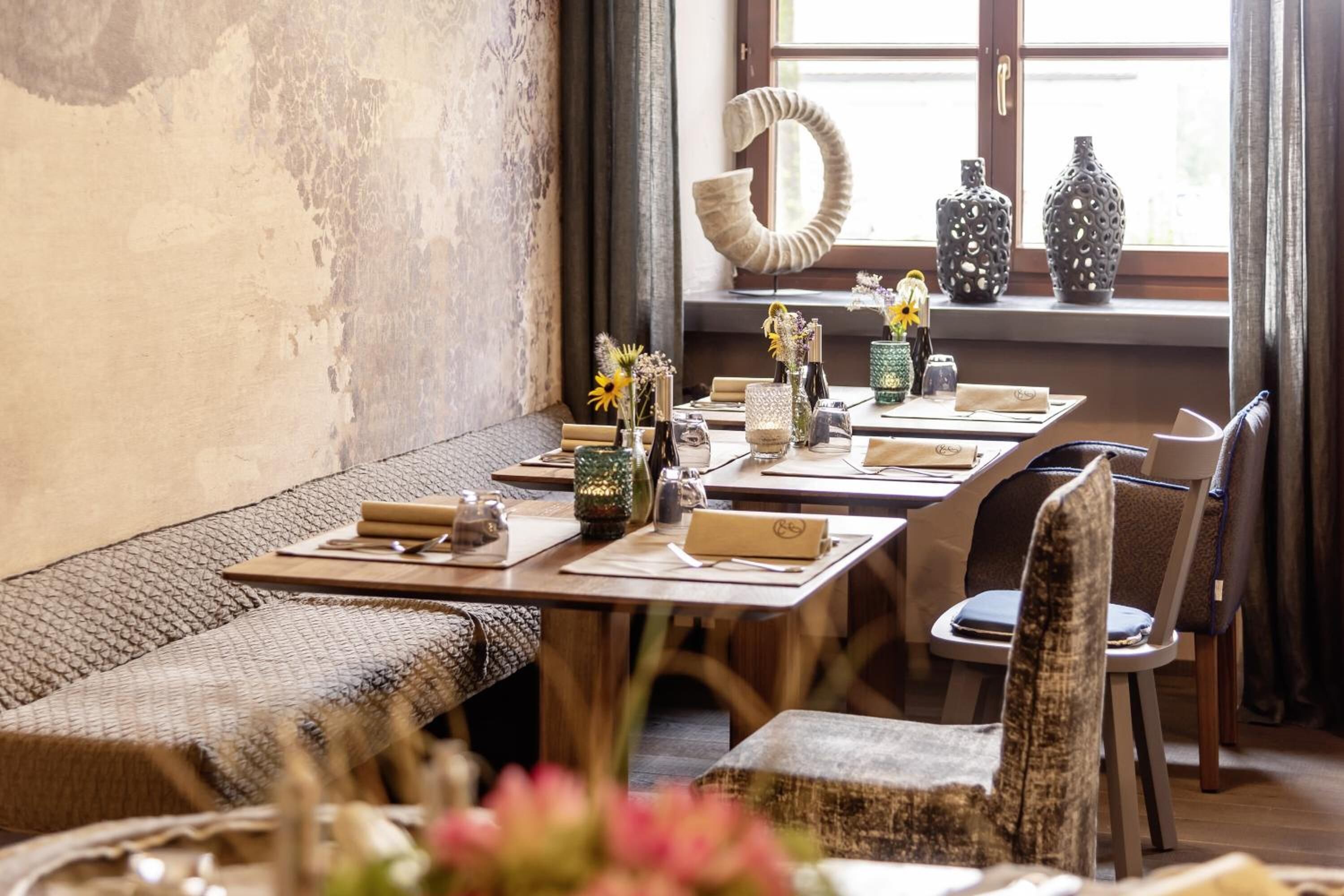 Un comedor con mesas de madera, asientos acolchados y jarrones decorativos.