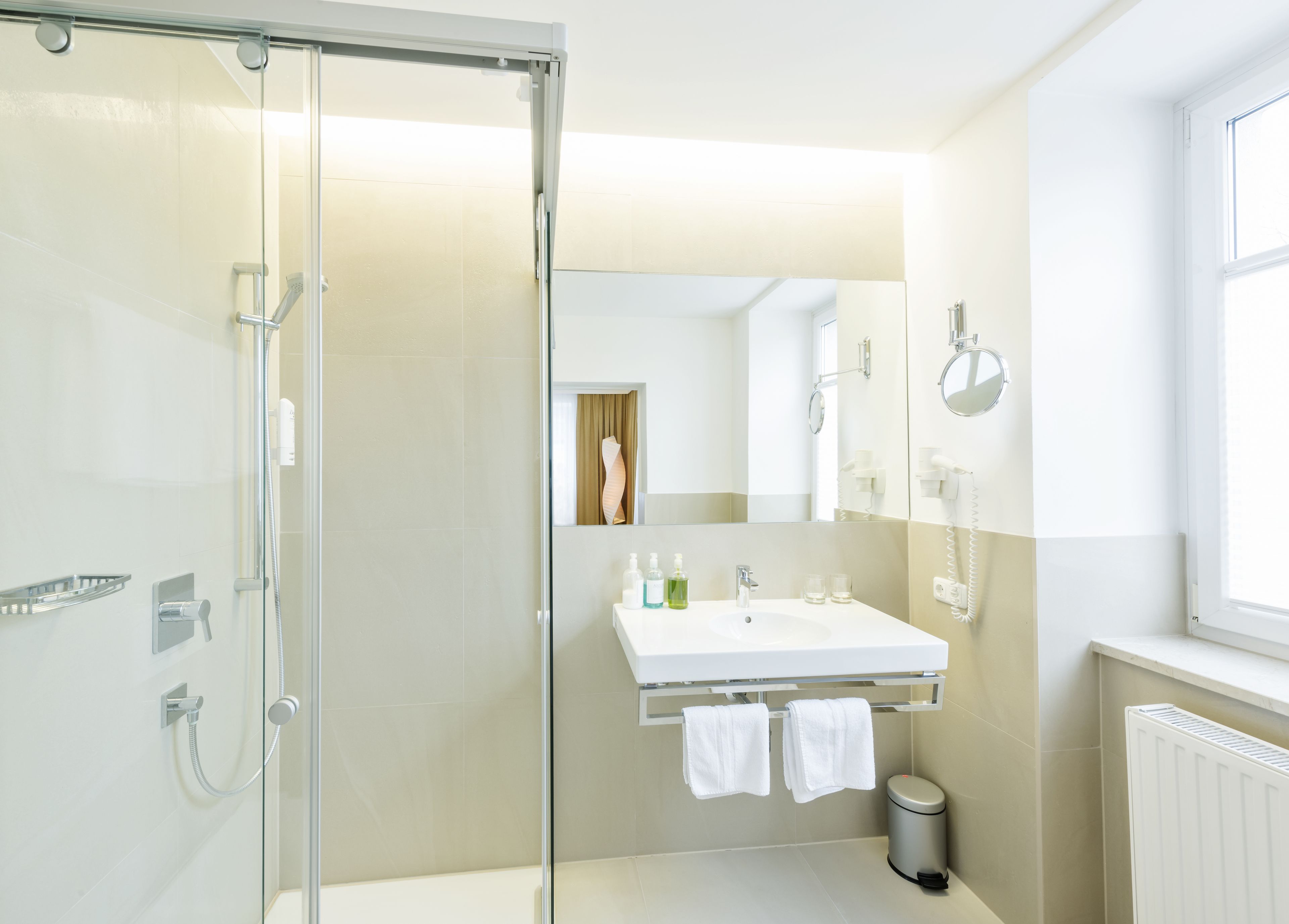 A modern bathroom with a glass shower enclosure, a white sink with a mirror above, and a radiator on the wall.