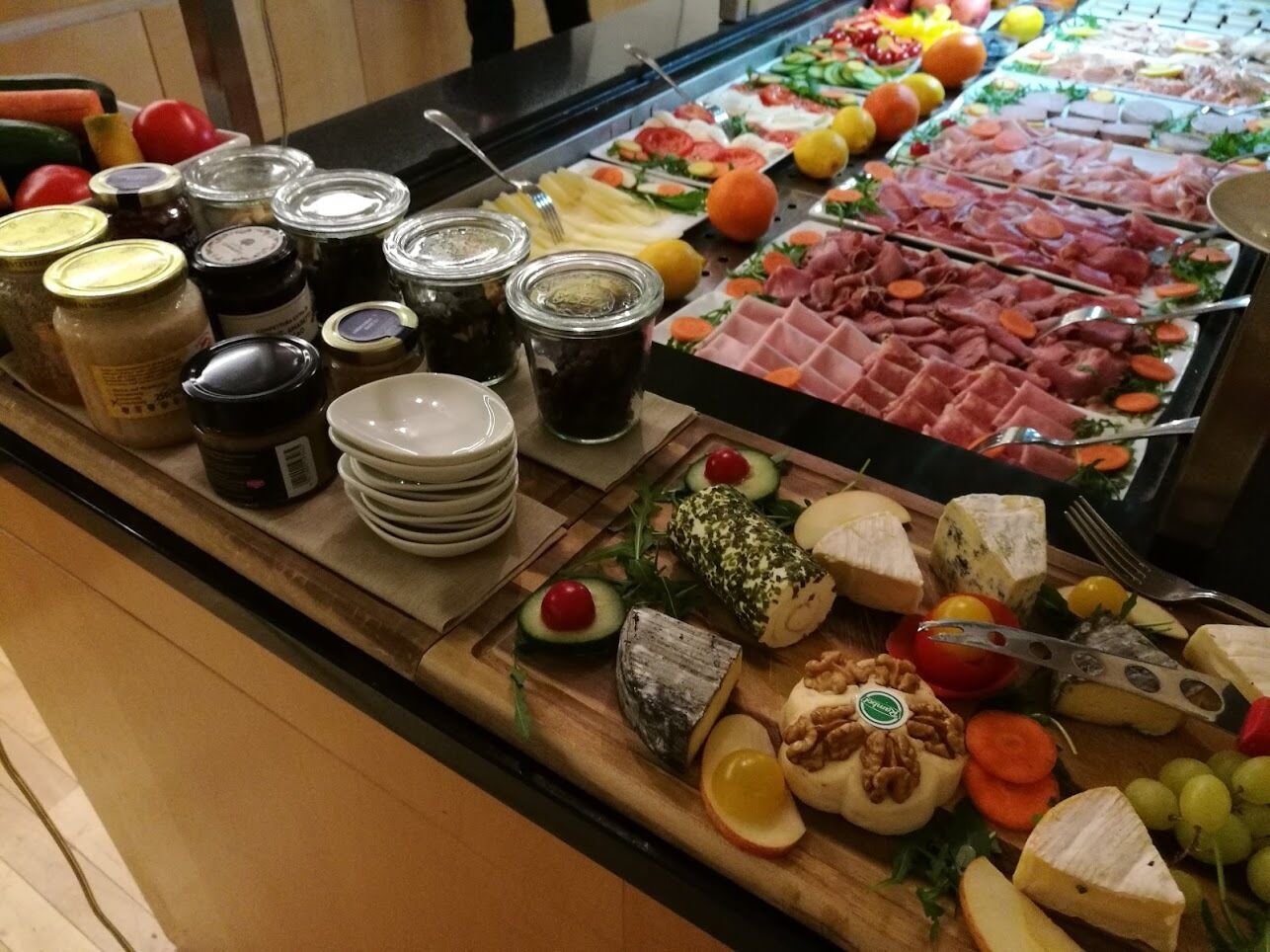 A buffet with various cheeses, meats, fruits, and condiments.