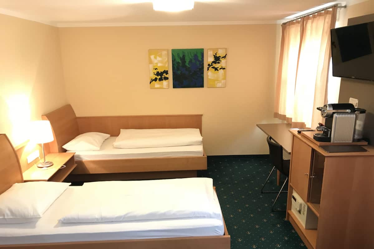 A hotel room with two beds, a desk, a TV, and artwork on the wall.