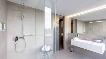 Uma casa de banho moderna com cabine de duche em vidro, um espelho grande e toucador branco com lavatório.
