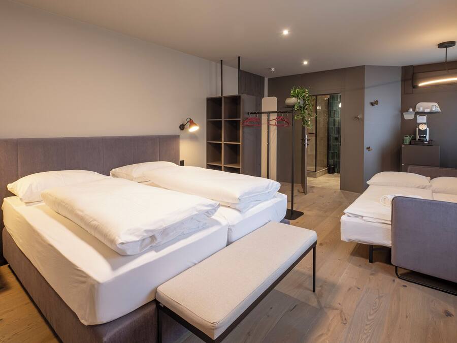 Ein Hotelzimmer mit Bett, Sitzbank, Stuhl, Nachttisch, Spiegel, Duschbereich und Kleiderschrank.