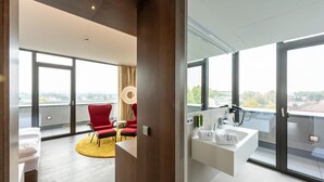 A modern hotel room with a large window, a red chair, a yellow rug, and a white sink.