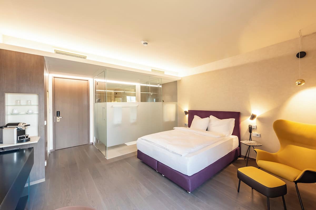 A modern hotel room with a bed, a desk, a chair, and a small table.