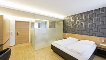 Une chambre d’hôtel moderne équipée d’un lit, d’une table de chevet et d’une douche séparée par des parois en verre.