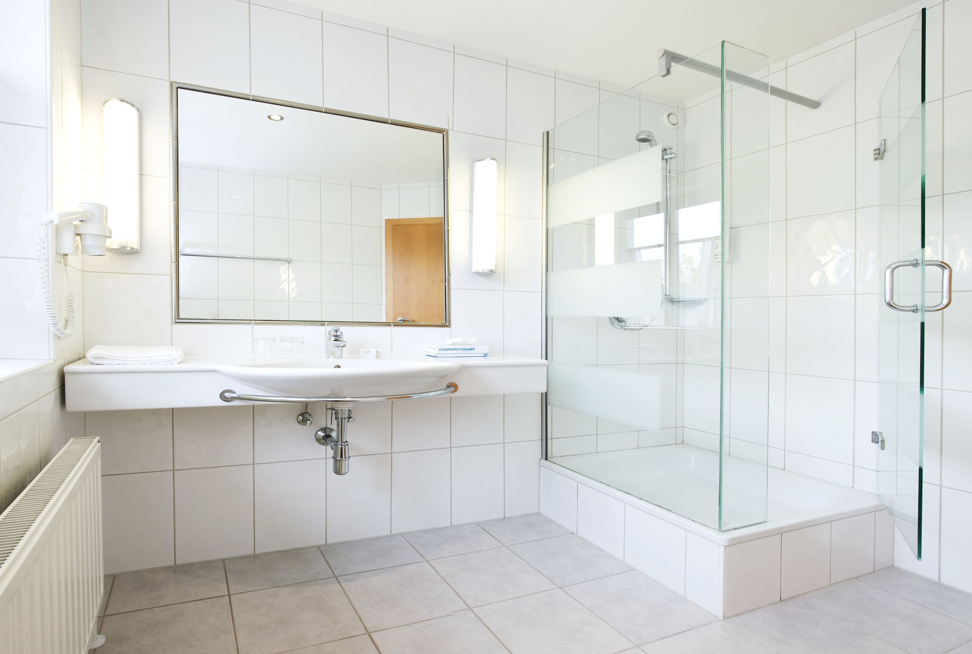 A modern bathroom with a glass-enclosed shower, a white sink with a mirror, and a towel rack.