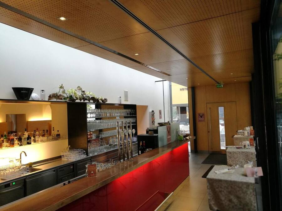 A hotel bar with a red counter, shelves of glasses, and a visible exit sign.