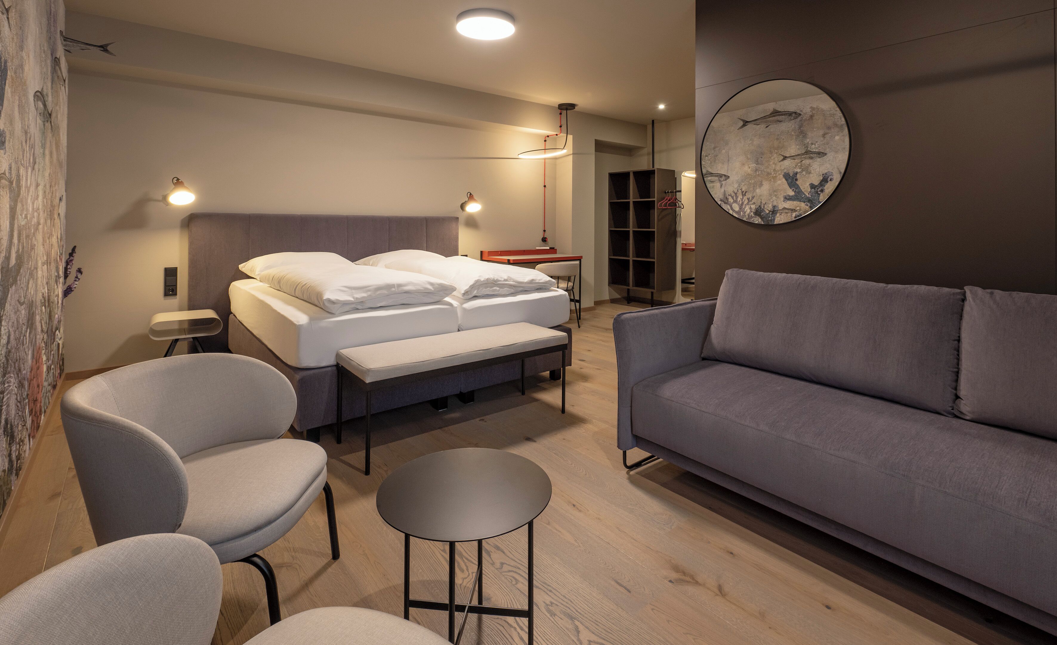A modern bedroom with a bed, two chairs, a sofa, a round table, and a wall art piece.