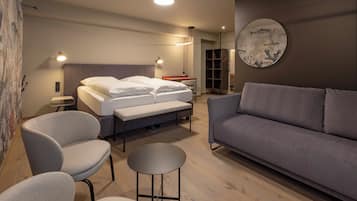 Et moderne soveværelse med en seng, to stole, en sofa, et rundt bord og et kunstværk på væggen.