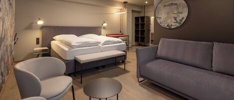 A modern bedroom with a bed, two chairs, a sofa, a round table, and a wall art piece.