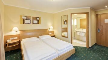 A hotel room with a double bed, bedside tables, a mirror, a small bedside lamp, and a bathroom visible through an open door.