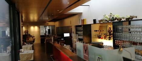 A bar area with a long counter, seating, and a display of glasses and bottles.