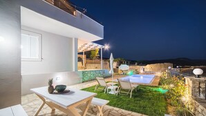 Un patio moderno al aire libre con piscina, suelo de piedra y una zona de comedor con mesa y sillas.