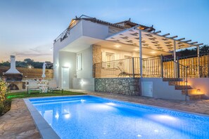 A modern house with a swimming pool, stone walls, and a covered outdoor area with stairs.