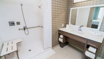 Ein modernes Badezimmer mit einer barrierefreien Dusche, einem Waschtisch mit großem Spiegel und einem Handtuchhalter.