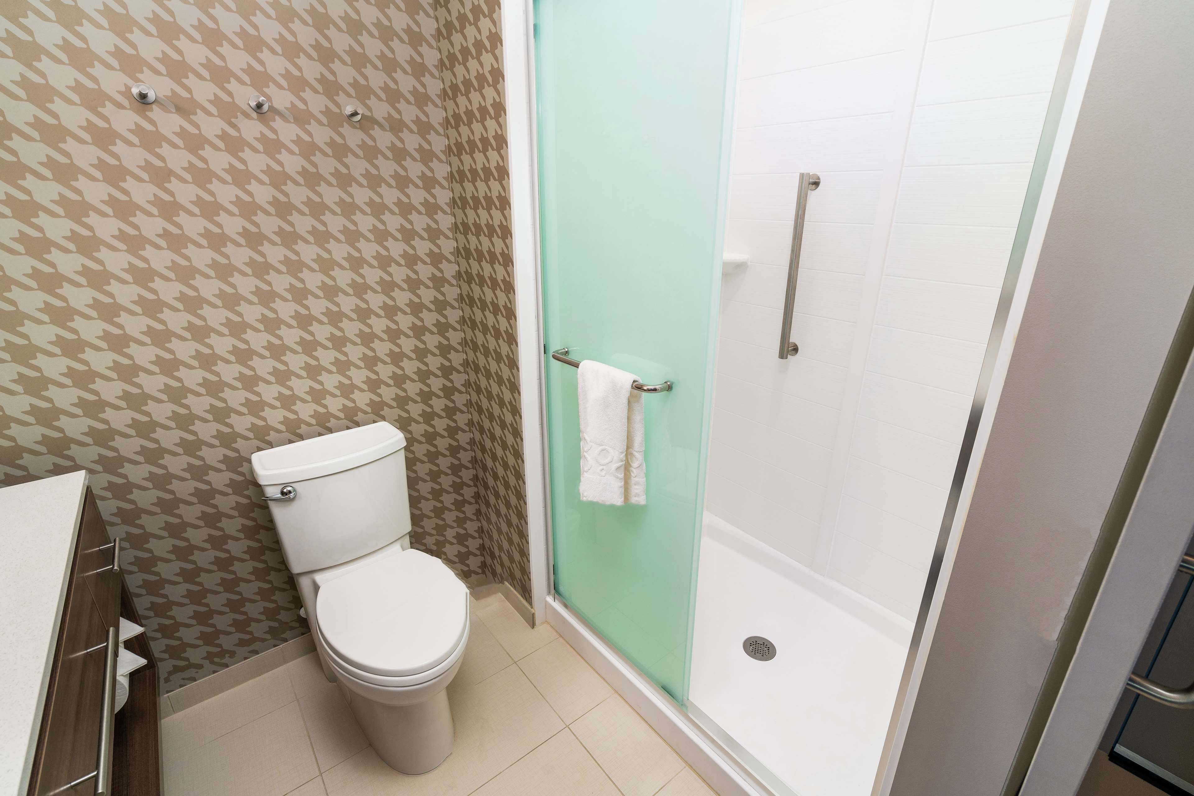Une salle de bain avec des toilettes, une douche dotée d’une porte en verre et un papier peint à motifs.