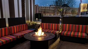 An outdoor seating area with a fire pit, surrounded by striped sofas, and a view of a building in the background. - Home2 Suites by Hilton Las Vegas Stadium District (Las Vegas)