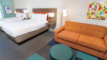 Quarto de hotel com uma cama grande, um sofá, um banquinho redondo e uma parede com uma pintura abstrata colorida.
