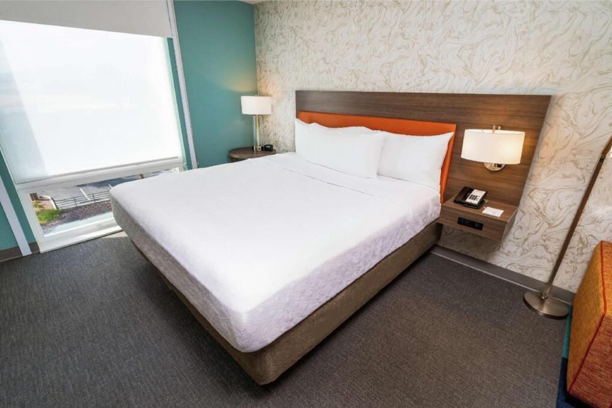 A hotel room with a large bed, two bedside tables with lamps, a window, and a patterned wall.