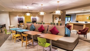 A modern restaurant with a long communal table, cushioned seating, and hanging pendant lights. - Home2 Suites by Hilton Las Vegas Stadium District (Las Vegas)