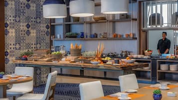 Un comedor moderno con una isla central, sillas blancas y un chef al fondo.