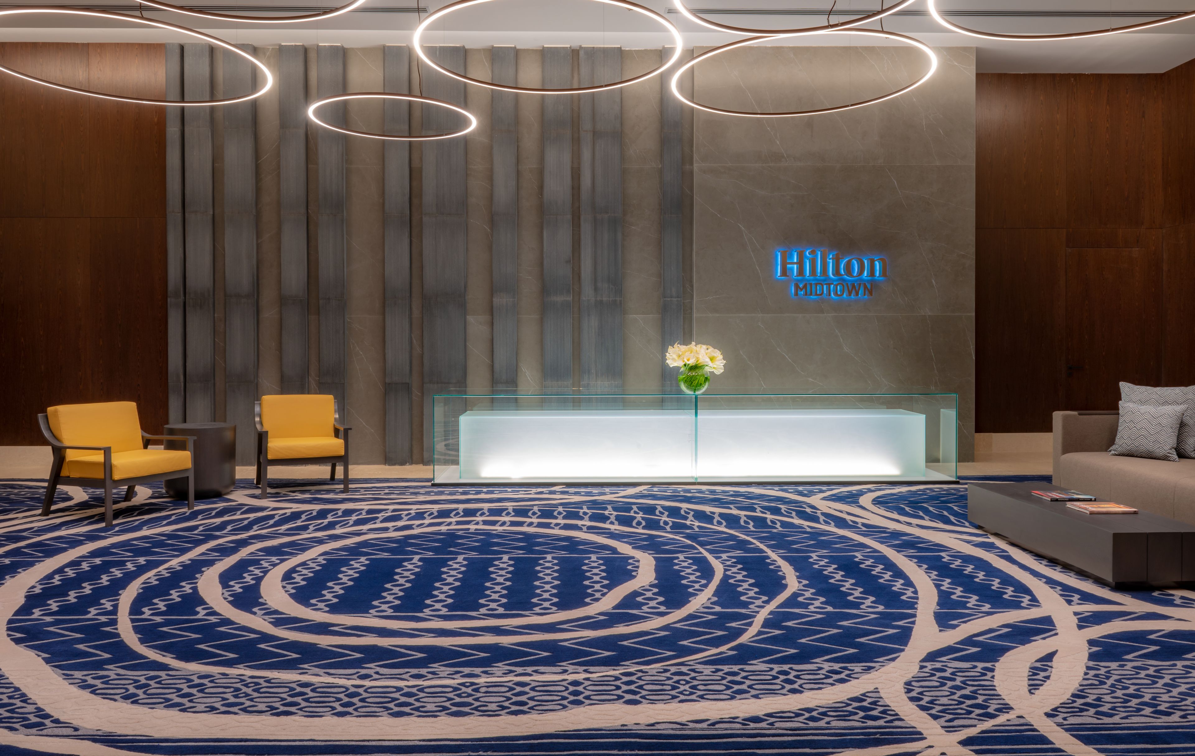 Un moderno vestíbulo de hotel con una recepción, una alfombra estampada en azul y un letrero de neón.