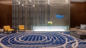 Un moderno vestíbulo de hotel con una recepción, una alfombra estampada en azul y un letrero de neón.
