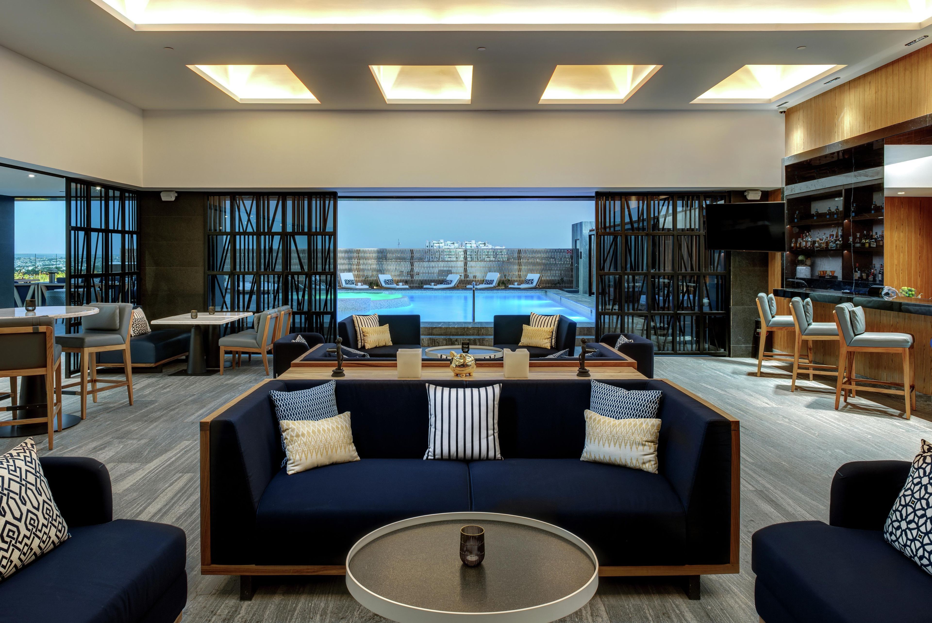 A modern lounge area with a pool view, seating arrangements, and a bar.